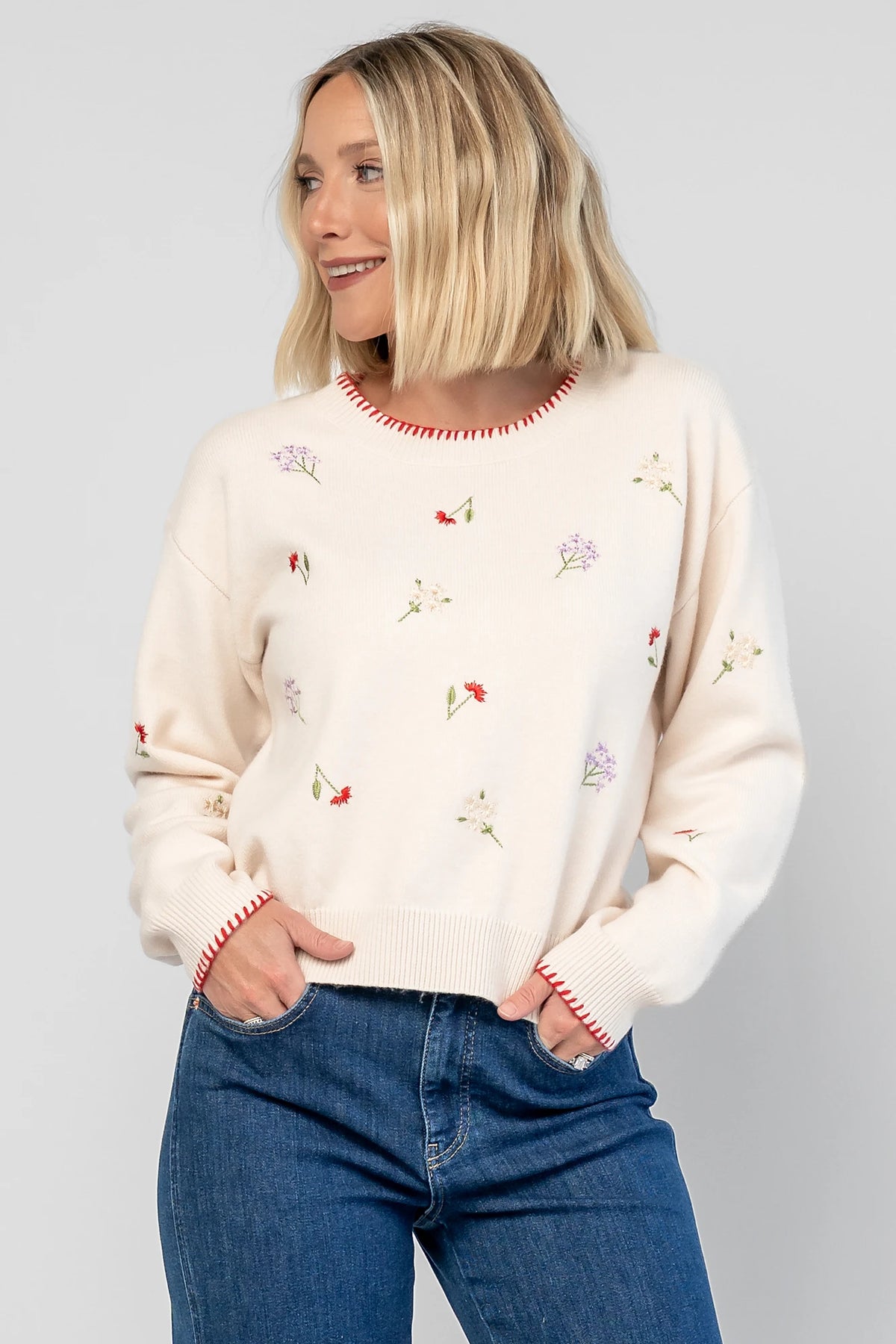 Ottilie Sweater in Cream with embroidered floral details, round neckline, red knit piping, and long sleeves.