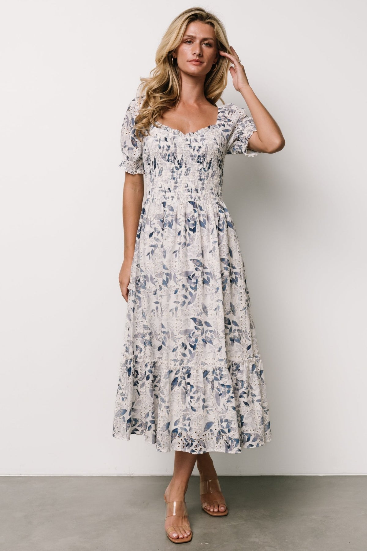 Three-quarter view of off-white dress showing raglan puff sleeve, smocked cuff, and delicate blue floral eyelet pattern across bodice.