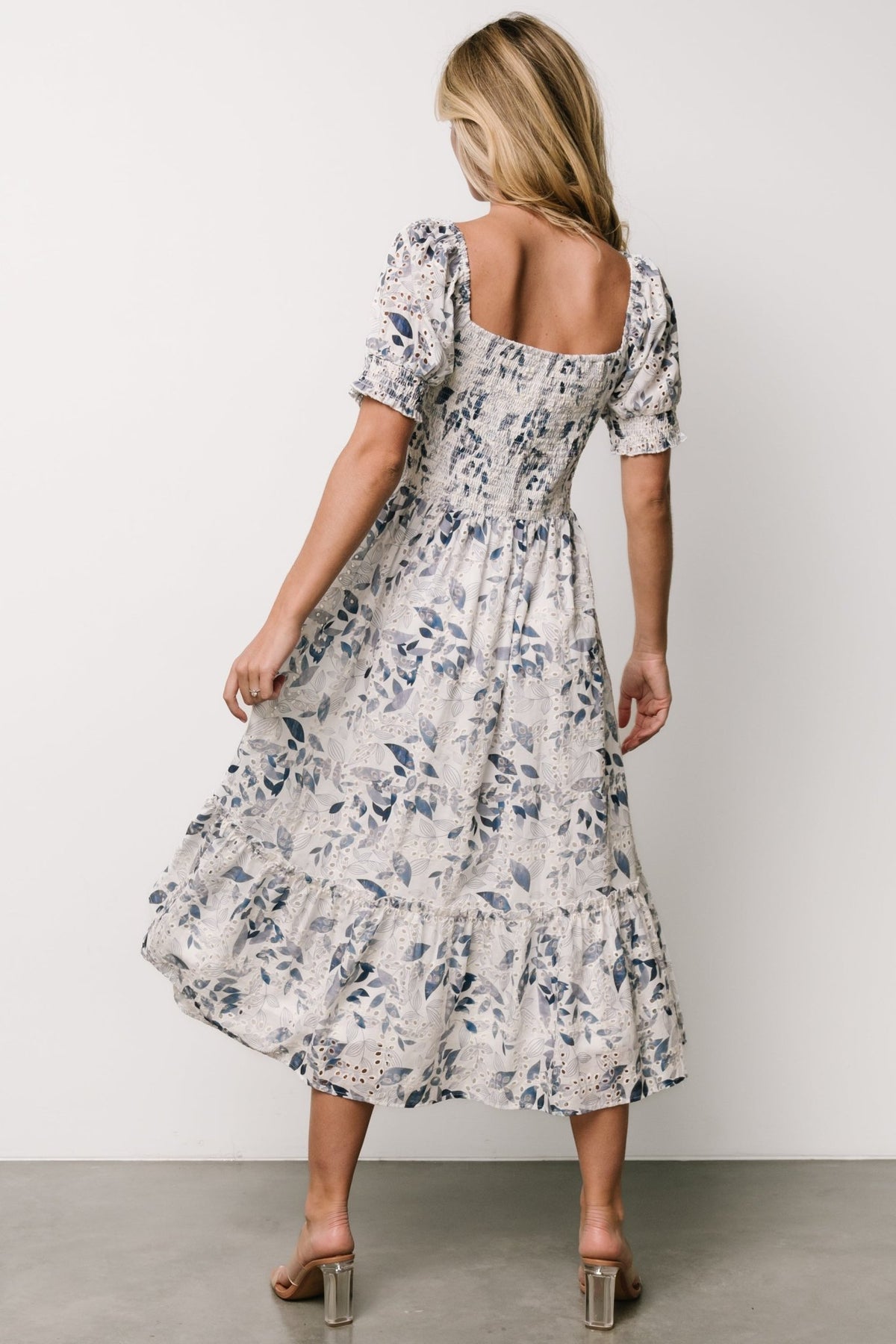 Side view highlighting natural-high waist, single ruffle-bordered tier and soft drape of the off-white dress with blue florals.