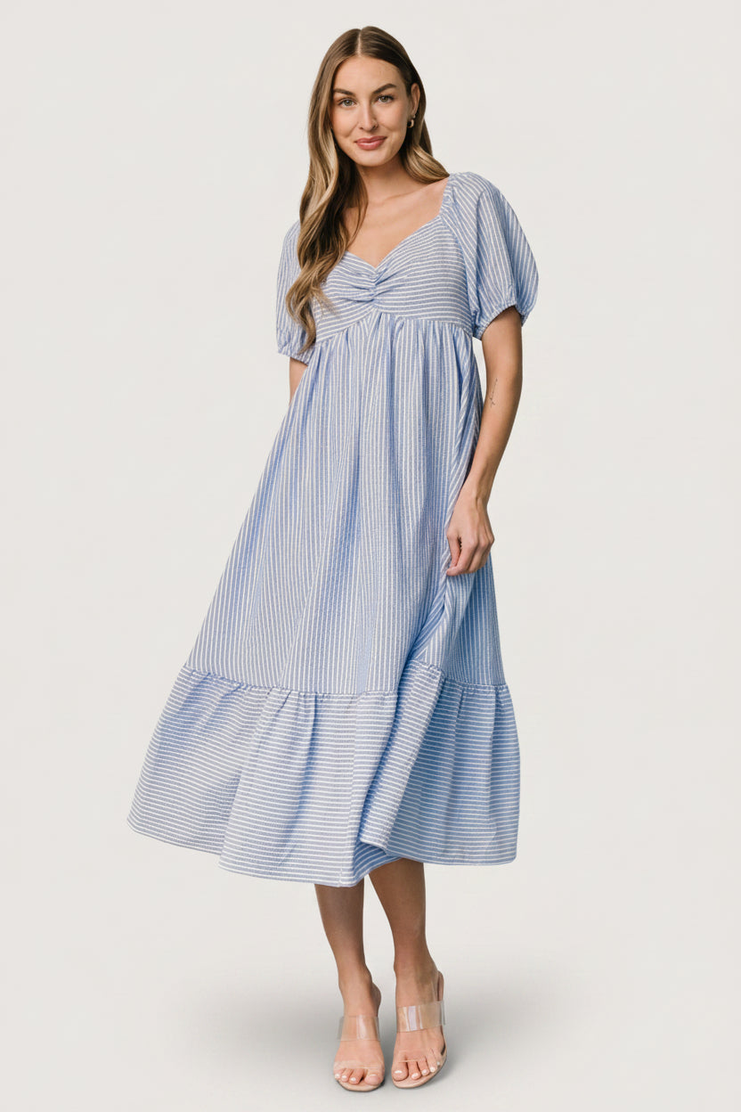 Model wearing Poppy Midi Dress in blue and off-white stripes, demonstrating fit at the empire waist, smocked back, and side pockets.