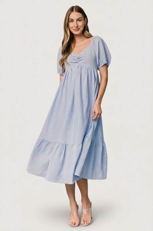 Model wearing Poppy Midi Dress in blue and off-white stripes, demonstrating fit at the empire waist, smocked back, and side pockets.