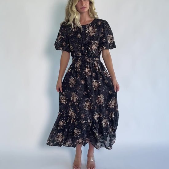 Model wearing a black floral midi dress with a round neckline, puff sleeves, and a smocked waist.