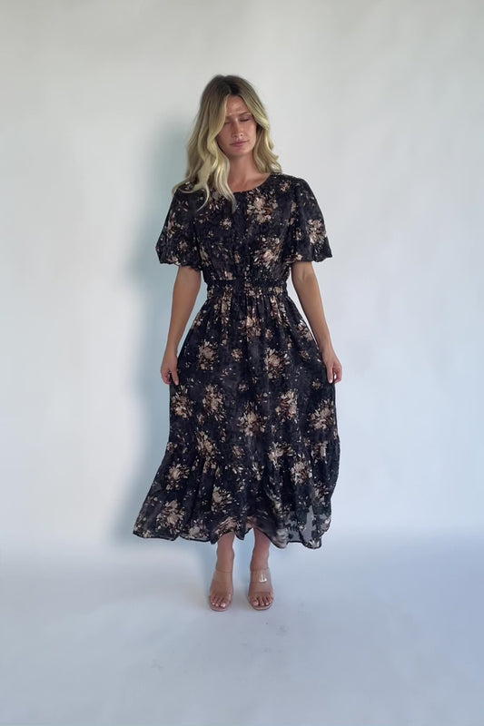 Model wearing a black floral midi dress with a round neckline, puff sleeves, and a smocked waist.