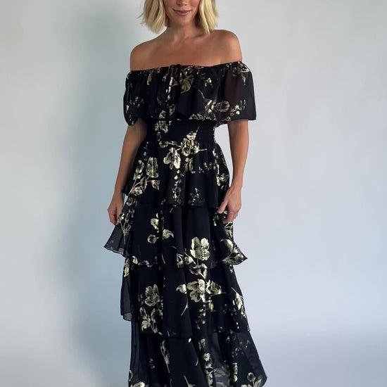 Carina Off Shoulder Maxi Dress in Black + Gold with floral print, ruffle neckline, smocked waist, and tiered chiffon skirt.