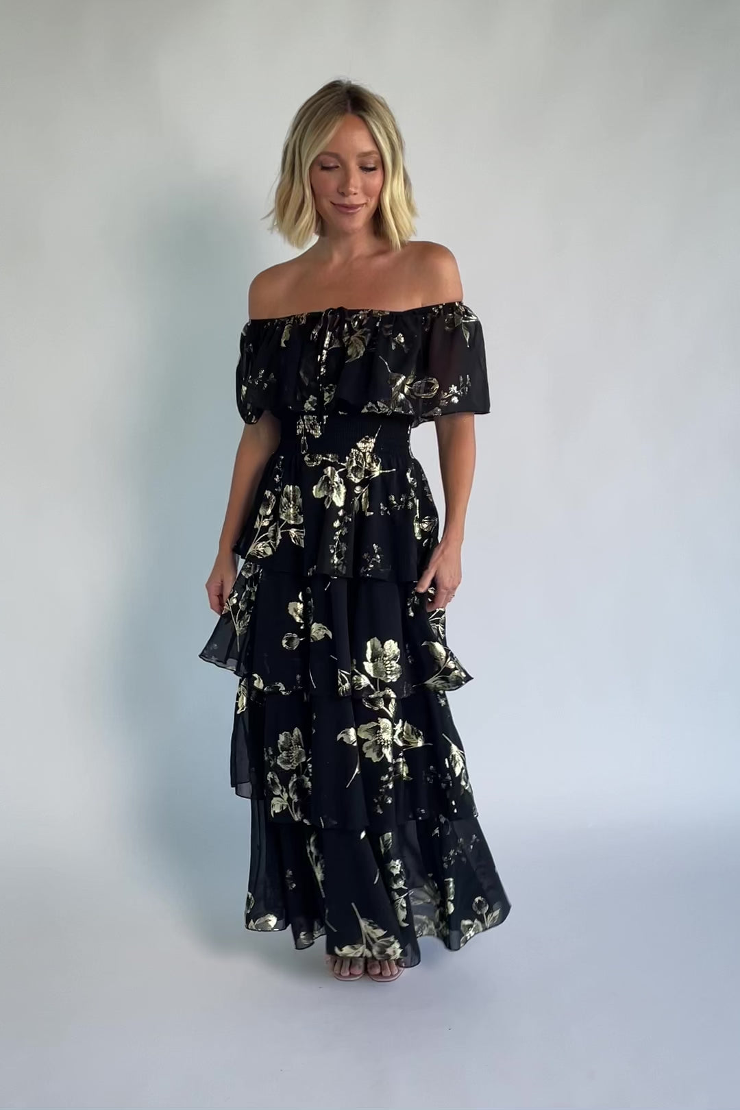 Carina Off Shoulder Maxi Dress in Black + Gold with floral print, ruffle neckline, smocked waist, and tiered chiffon skirt.