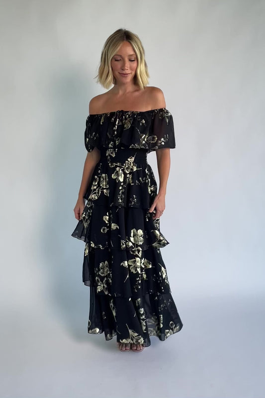 Carina Off Shoulder Maxi Dress in Black + Gold with floral print, ruffle neckline, smocked waist, and tiered chiffon skirt.