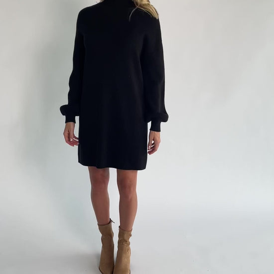 Black knit sweater dress with a mock neckline, long balloon sleeves, dropped shoulders, and a relaxed above-the-knee silhouette.