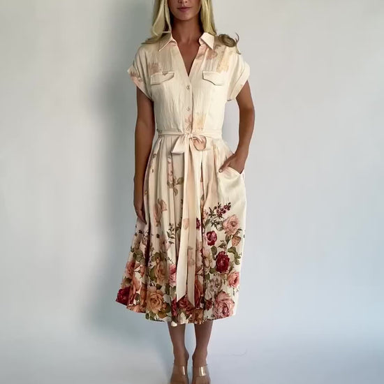Model wearing a cream floral midi dress with a collared neckline, functional button-front bodice, short sleeves, a removable waist tie, and a flowing midi-length skirt.