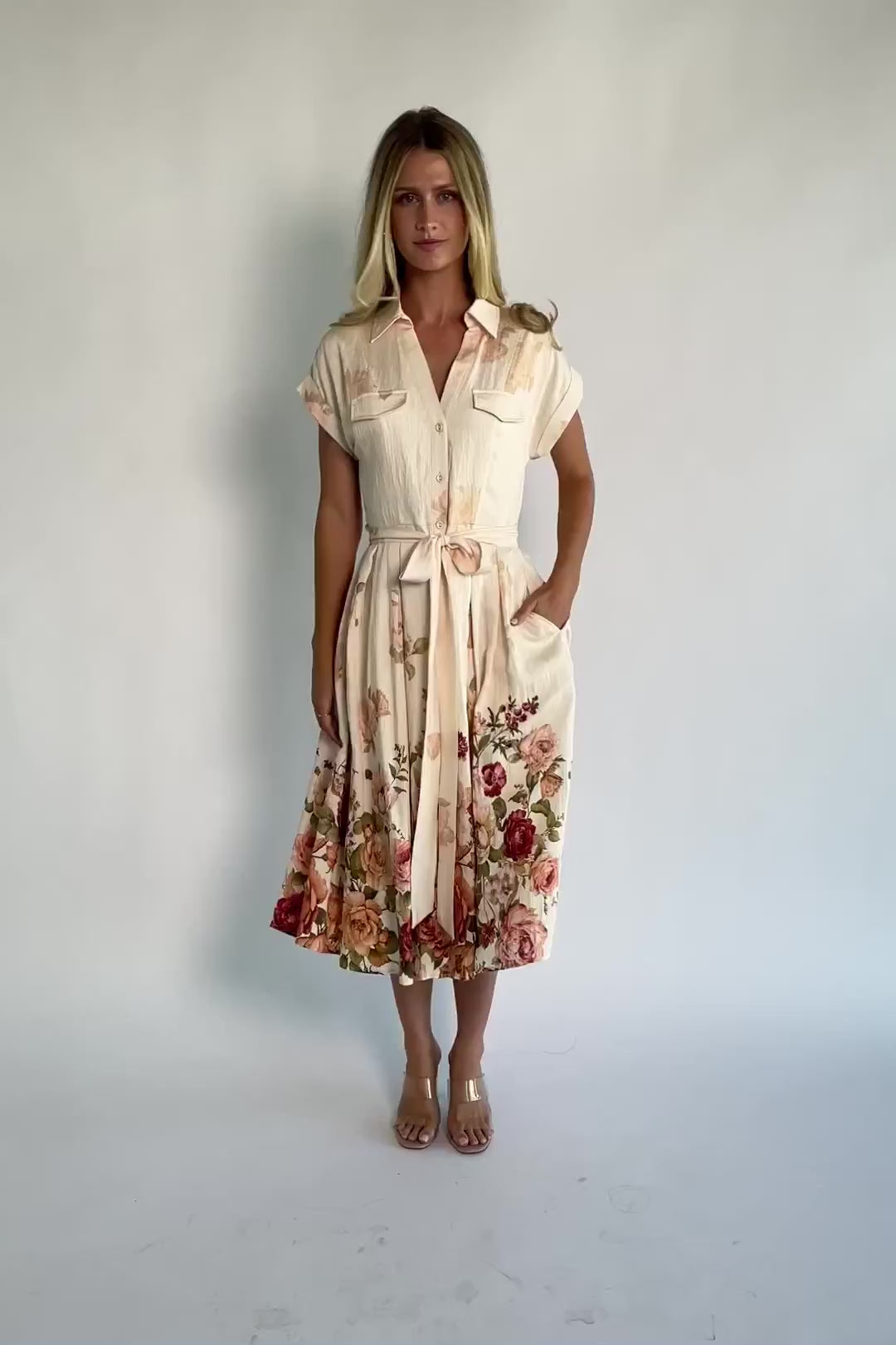 Model wearing a cream floral midi dress with a collared neckline, functional button-front bodice, short sleeves, a removable waist tie, and a flowing midi-length skirt.