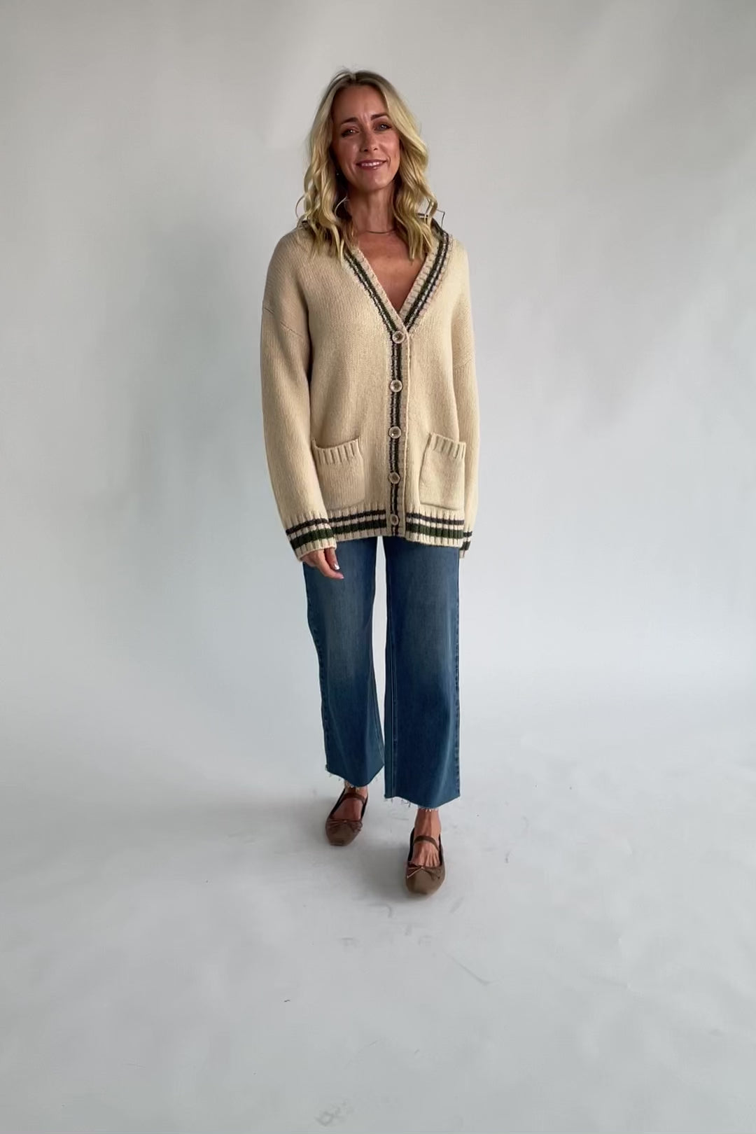 Oatmeal knit cardigan with a V-neckline, button-front closure, olive and charcoal striped trim, front patch pockets, and a relaxed fit.