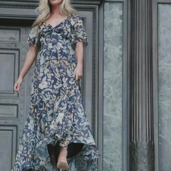 Navy floral chiffon maxi dress with a sweetheart neckline, knot detail, flutter sleeves, smocked back bodice, and a flowing tiered skirt.