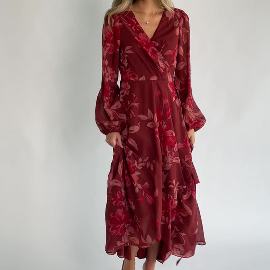 Rust multi floral chiffon maxi dress with a faux wrap neckline, long balloon sleeves, adjustable waist tie, and a high-low skirt.
