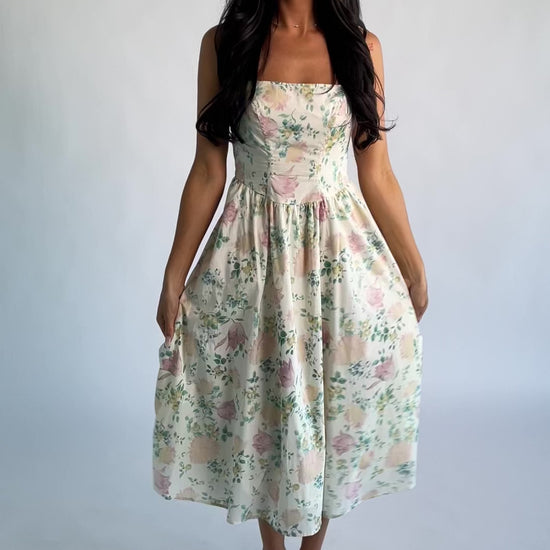 Model wearing a cream floral midi dress with a square neckline, adjustable shoulder tie straps, fitted bodice, and flowing skirt. 