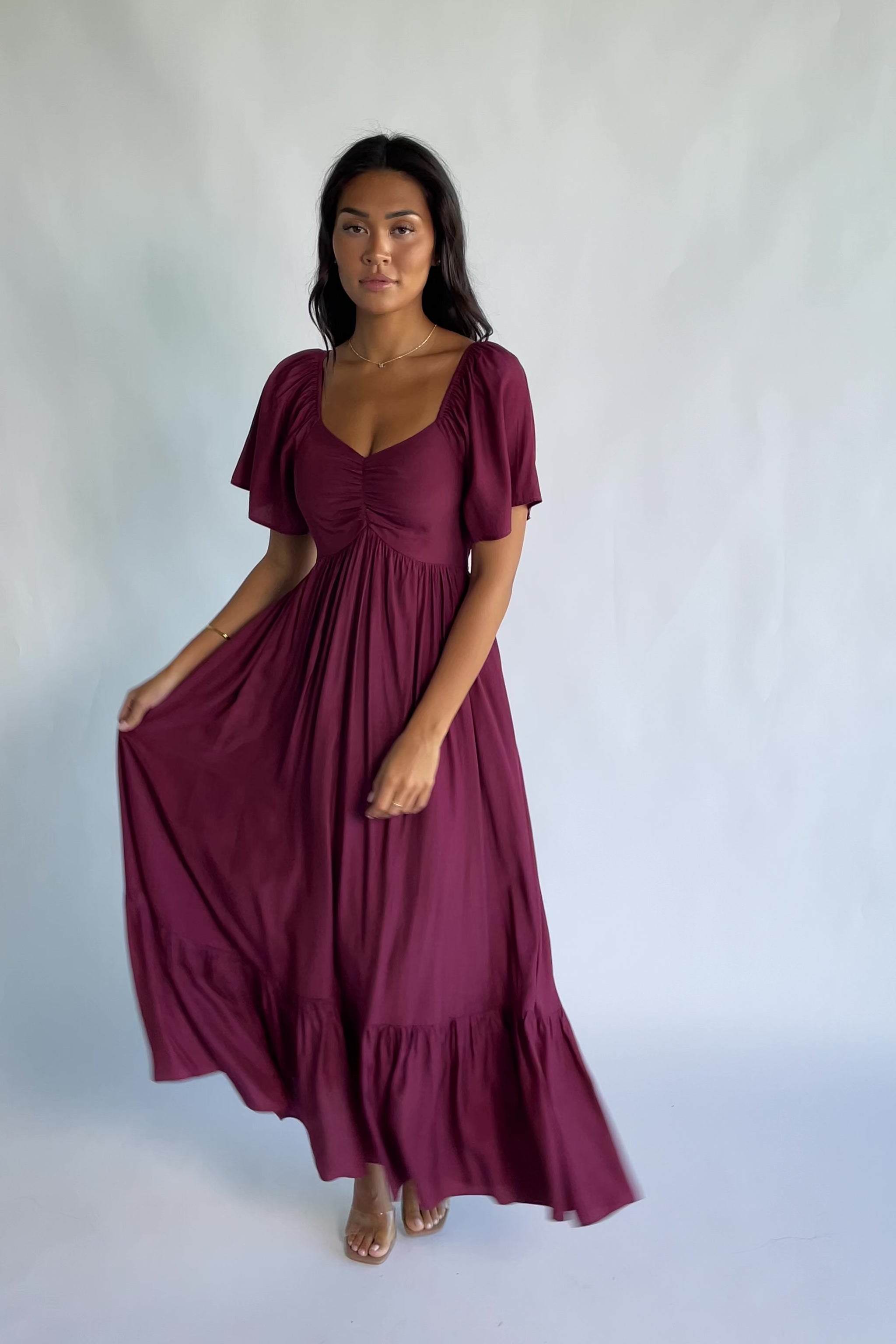 Anisa Midi Dress in Burgundy with a wide V-neckline, cinched bust, elastic shoulders, and a tiered skirt.