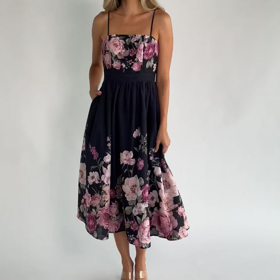 Black floral midi dress with a straight neckline, adjustable spaghetti straps, smocked back, gathered skirt, and side pockets.