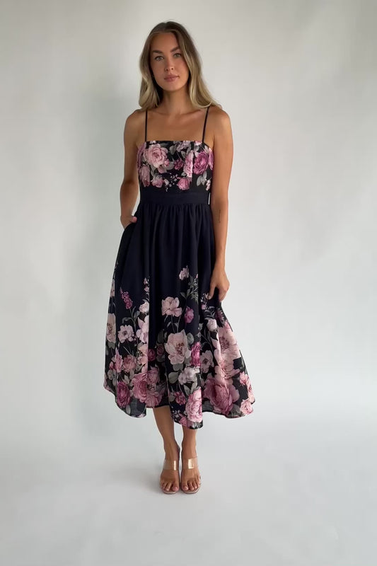 Black floral midi dress with a straight neckline, adjustable spaghetti straps, smocked back, gathered skirt, and side pockets.