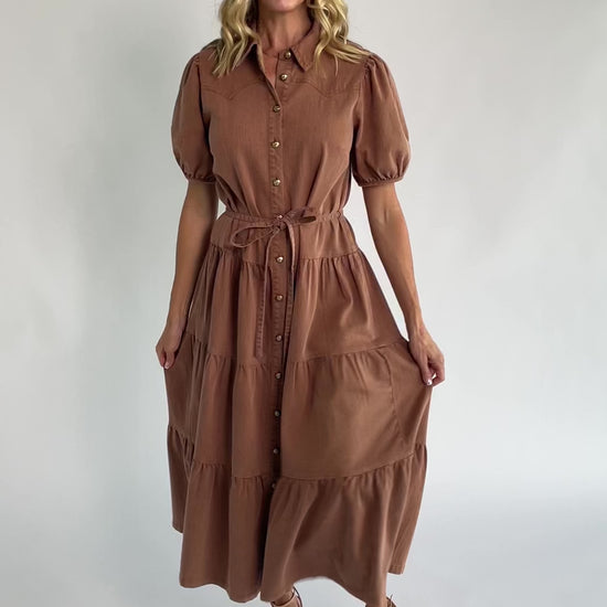 Dusty mocha midi dress with a collared neckline, gold-tone button-front closure, short puff sleeves, removable waist tie, and tiered skirt.