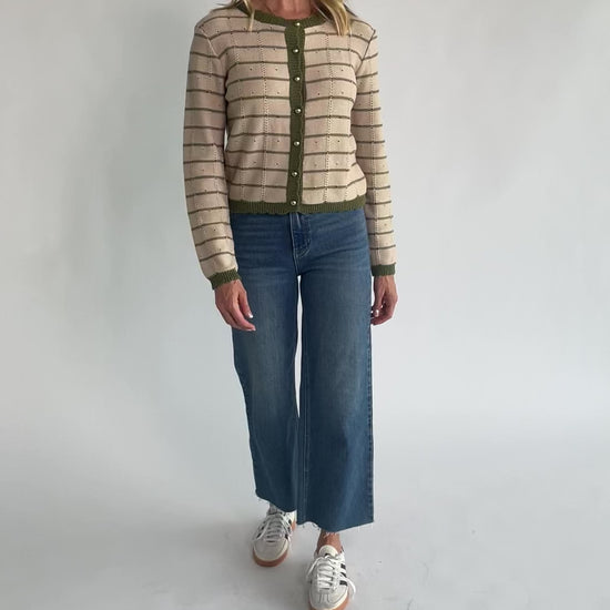 Beige pointelle knit cardigan with olive striped detailing, a round scalloped neckline, pearl-inspired button-front closure, long sleeves, and scalloped ribbed trim.