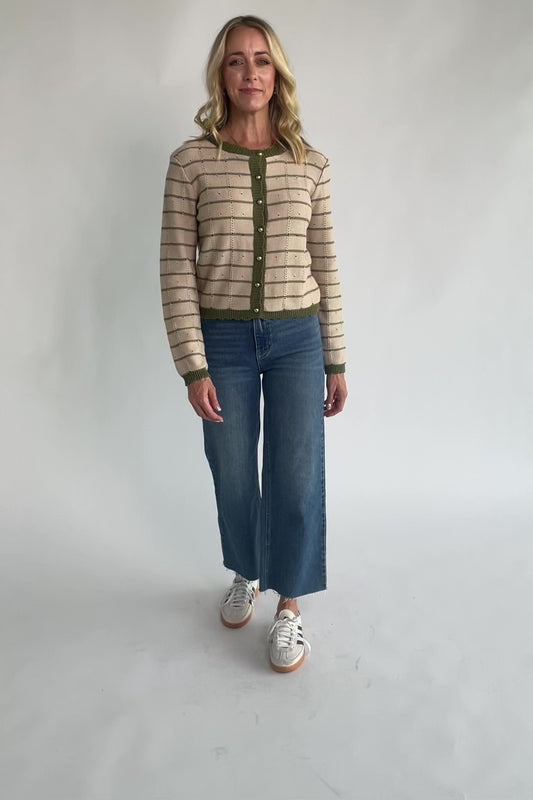 Beige pointelle knit cardigan with olive striped detailing, a round scalloped neckline, pearl-inspired button-front closure, long sleeves, and scalloped ribbed trim.