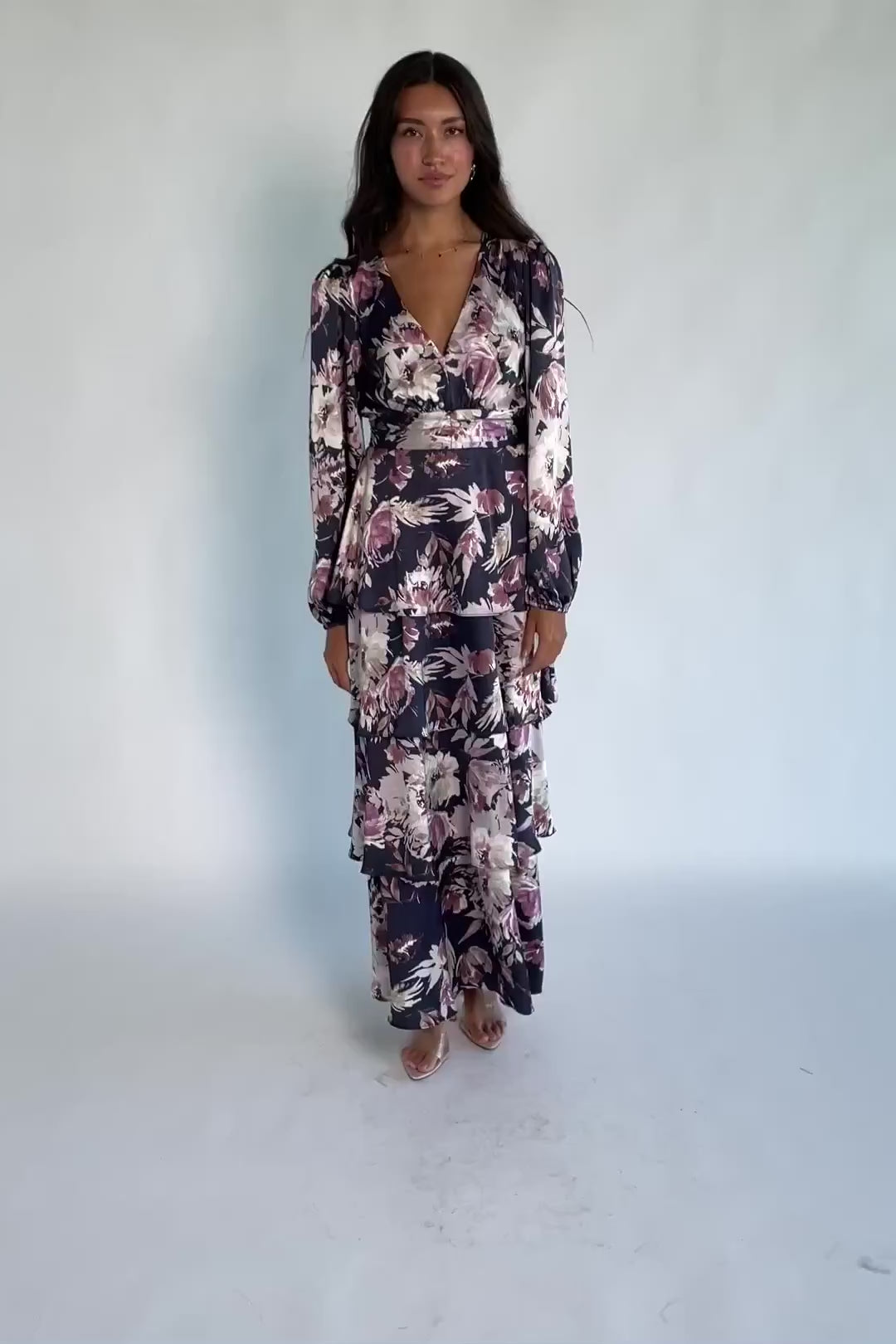 Model wearing the Montrouge Tiered Satin Maxi Dress in Navy + Lilac Floral featuring a V-neckline, short flutter sleeves, a smocked back, and a flowing tiered satin maxi skirt with a navy background and lilac floral print.
