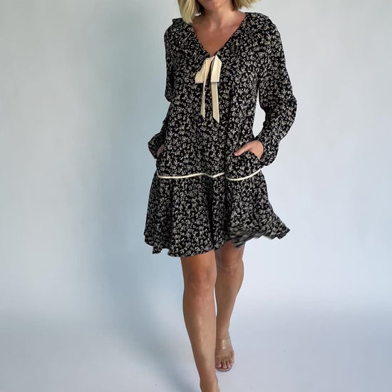 Shantel Bow Front Short Dress in Black Floral with ruffled neckline, faux bow front, long sleeves, and short skirt.