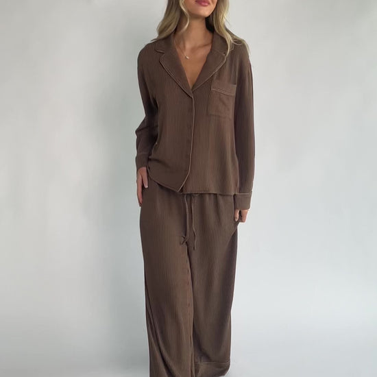 Brown ribbed pajama set with a button-front V-neck top, long sleeves, chest pocket, and wide-leg pants with an elastic drawstring waist.