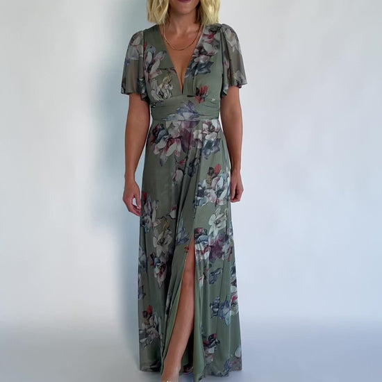 Model wearing a sage floral maxi dress with a deep V-neckline, short flutter sleeves, and an empire waist.