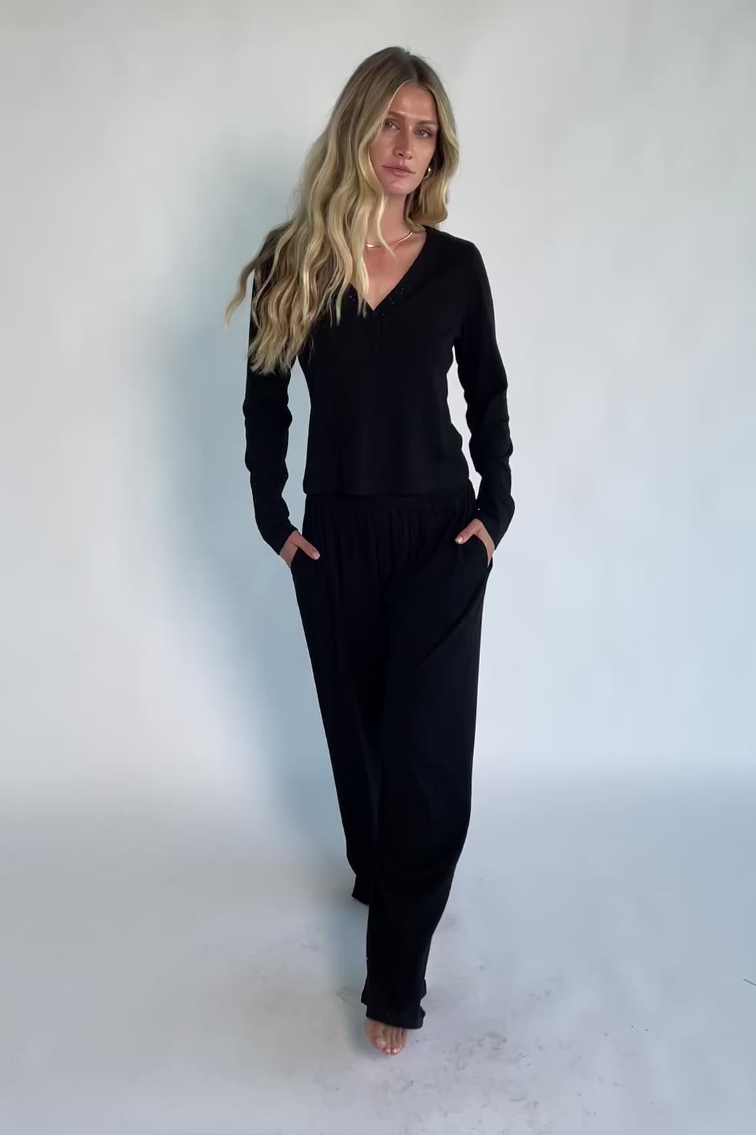 Model wearing the Rubi Soft Ribbed Pajama Set in Black featuring a soft ribbed knit, long-sleeve V-neck top with a snap-button placket, and matching straight-leg pants with an elastic waistband and side pockets.
