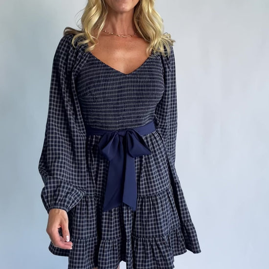 Stina Short Dress in Navy Plaid with smocked V-neck bodice, long sleeves, and tiered skirt.