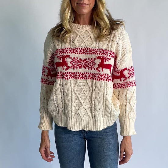 Elyse Sweater in Cream + Red with a Fair Isle reindeer and snowflake pattern, cable knit detailing, and a crew neckline.
