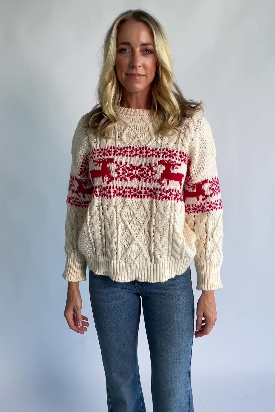 Elyse Sweater in Cream + Red with a Fair Isle reindeer and snowflake pattern, cable knit detailing, and a crew neckline.