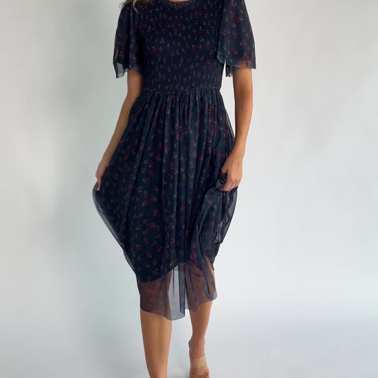 Navy floral mesh midi dress with a high ruffle neckline, flutter sleeves, full smocked bodice, and flowing midi skirt.