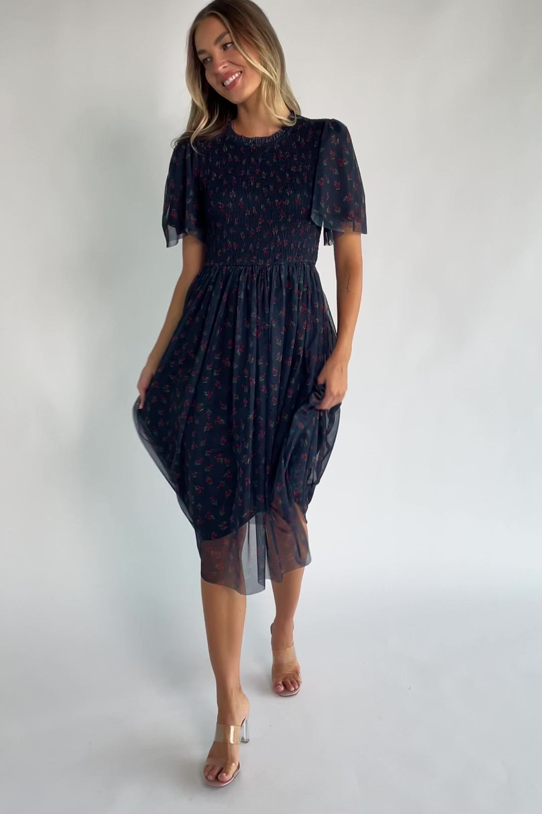 Navy floral mesh midi dress with a high ruffle neckline, flutter sleeves, full smocked bodice, and flowing midi skirt.
