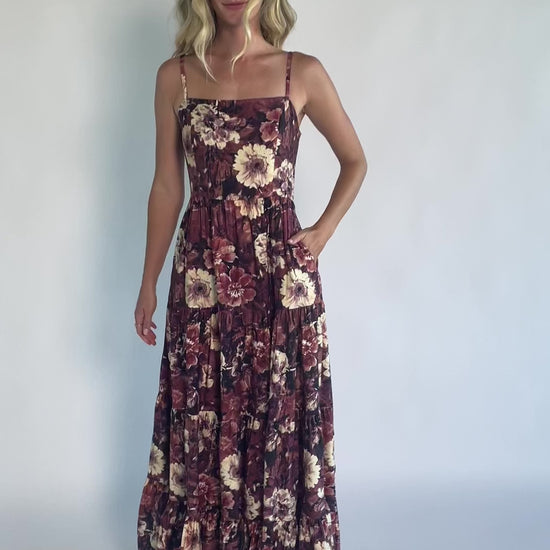 Model wearing a deep berry floral maxi dress with a square neckline, adjustable spaghetti straps, and a smocked back bodice.