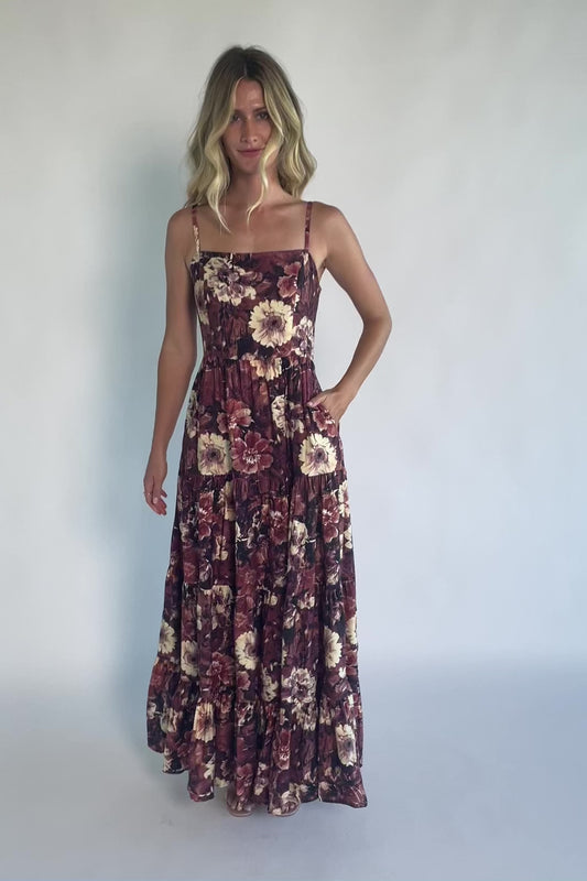 Model wearing a deep berry floral maxi dress with a square neckline, adjustable spaghetti straps, and a smocked back bodice.