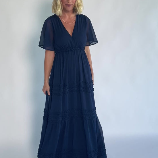 Model wearing a navy chiffon maxi dress with a surplice V-neckline, short ruffled sleeves, and an elastic empire waist.