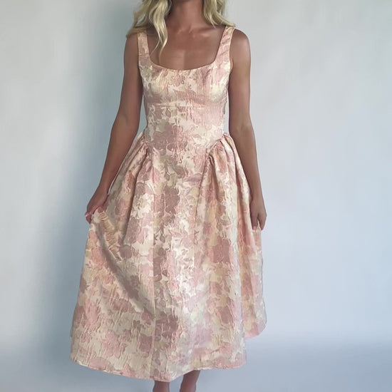 Model wearing a peach floral jacquard midi dress with a square neckline, wide tank straps, and a fitted bodice.