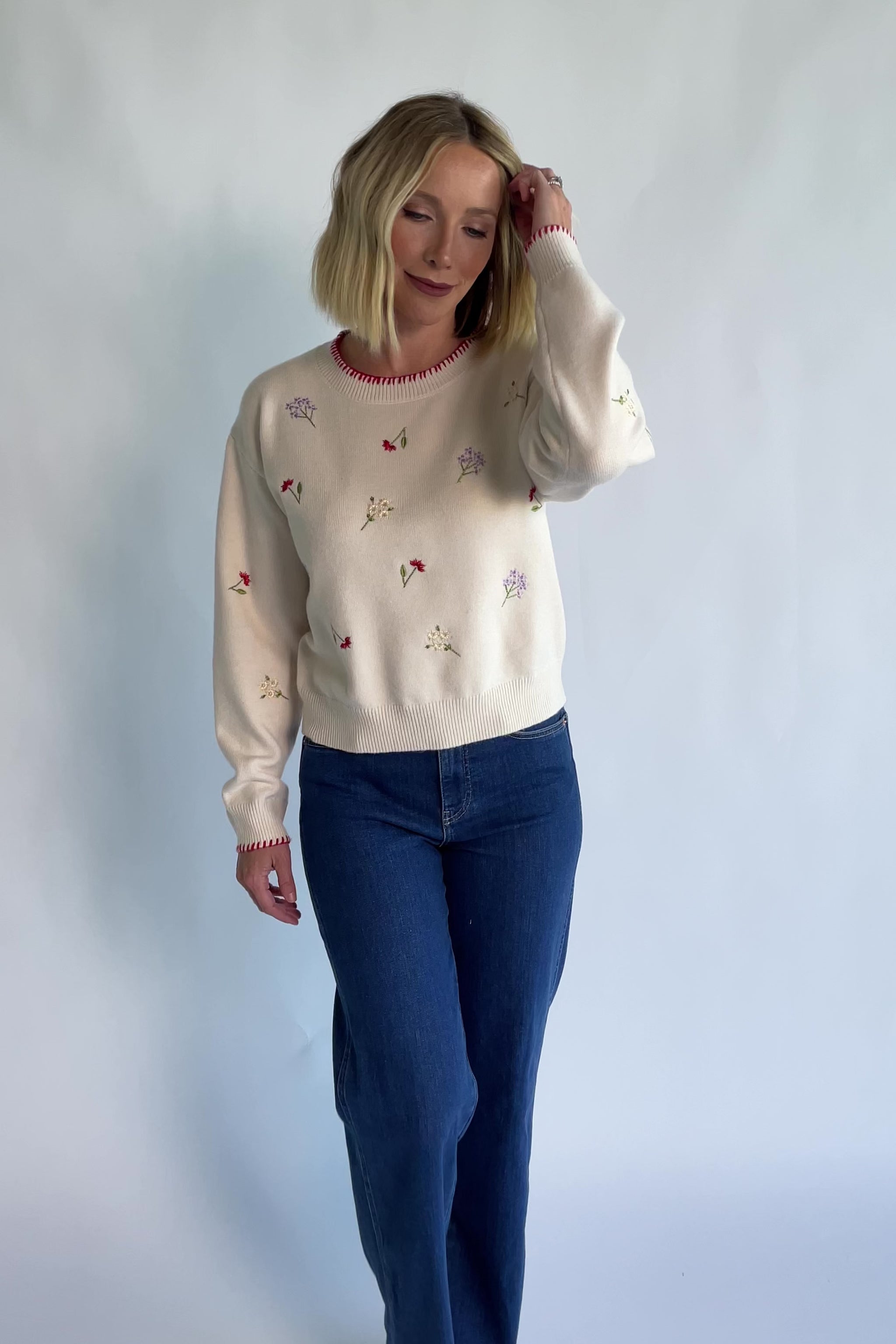 Ottilie Sweater in Cream with embroidered floral details, round neckline, red knit piping, and long sleeves.