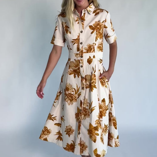 Model wearing the Selena Button Up Dress in Ivory + Golden Floral featuring a collared neckline, functional button-front closure, short sleeves, princess seams, and a fit-and-flare midi silhouette in stretch denim with an ivory background and golden floral print.