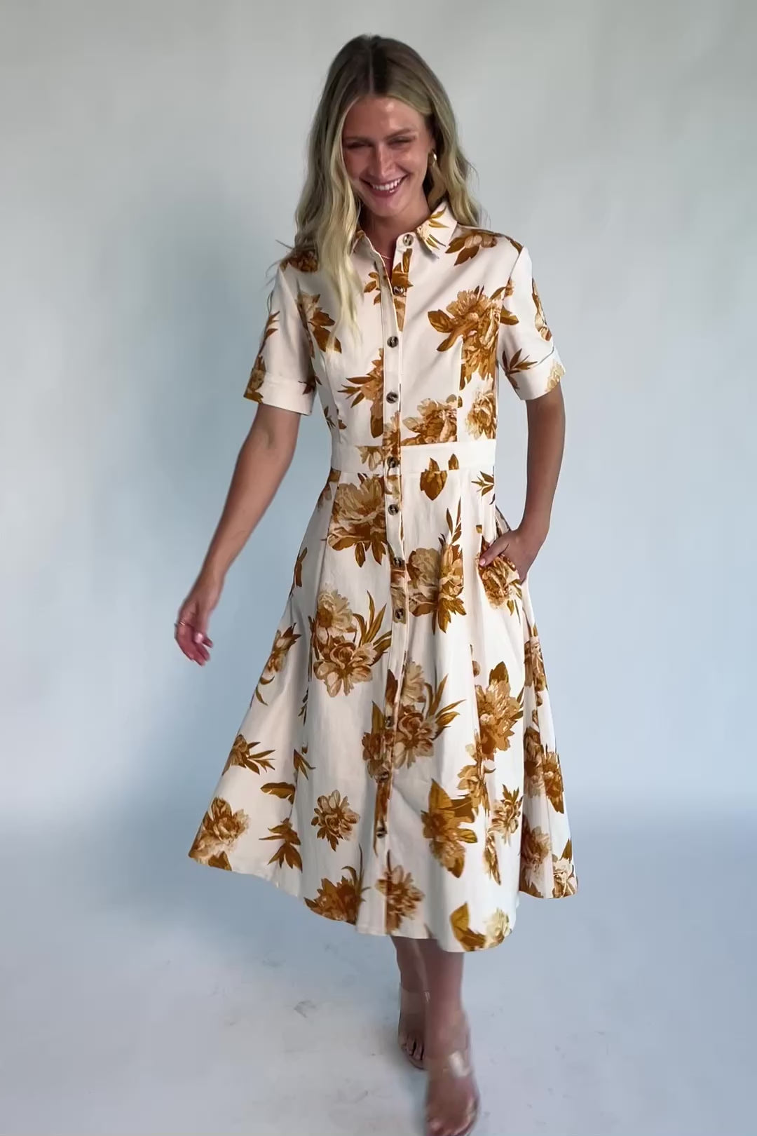 Model wearing the Selena Button Up Dress in Ivory + Golden Floral featuring a collared neckline, functional button-front closure, short sleeves, princess seams, and a fit-and-flare midi silhouette in stretch denim with an ivory background and golden floral print.