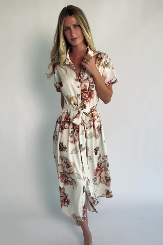Model wearing the Blythe Midi Dress in Ivory Floral featuring a collared neckline, functional button-front bodice, short rolled sleeves, and a removable waist tie.