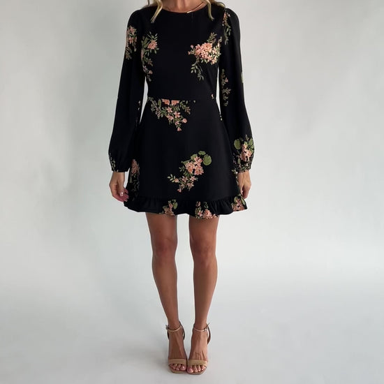 Black floral mini dress with a round neckline, long sleeves, fitted bodice, ruffle hem, back keyhole tie, and hidden back zipper.
