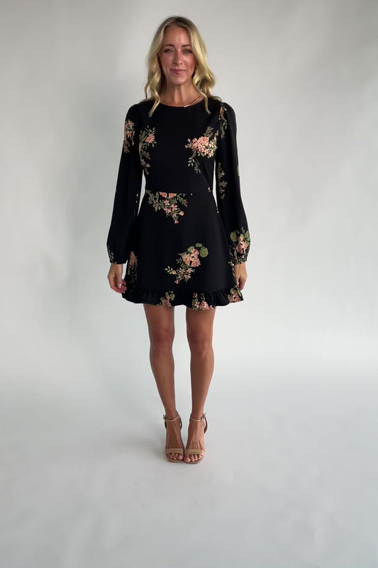 Black floral mini dress with a round neckline, long sleeves, fitted bodice, ruffle hem, back keyhole tie, and hidden back zipper.