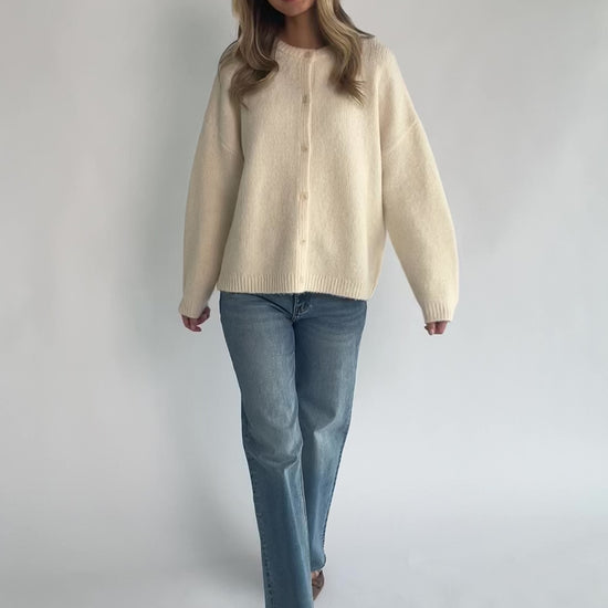 Cream fuzzy knit cardigan with a round neckline, button-front closure, long sleeves, dropped shoulders, and a relaxed fit.