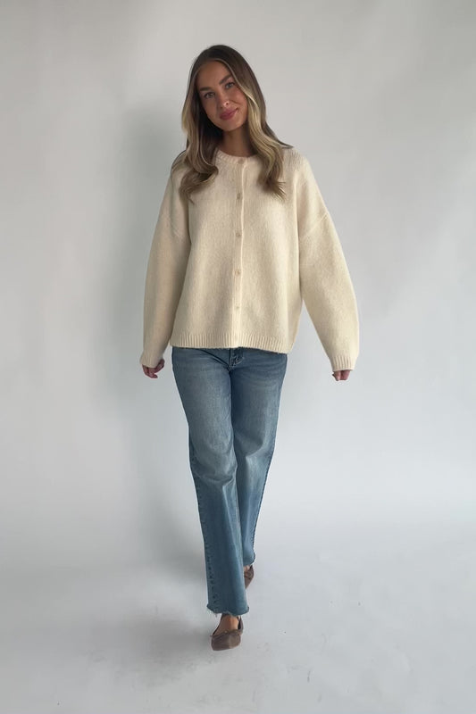 Cream fuzzy knit cardigan with a round neckline, button-front closure, long sleeves, dropped shoulders, and a relaxed fit.