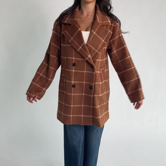 Cognac plaid mid-length coat with a cream windowpane pattern, tailored collar, button-front closure, long sleeves, front pockets, and a fully lined interior.