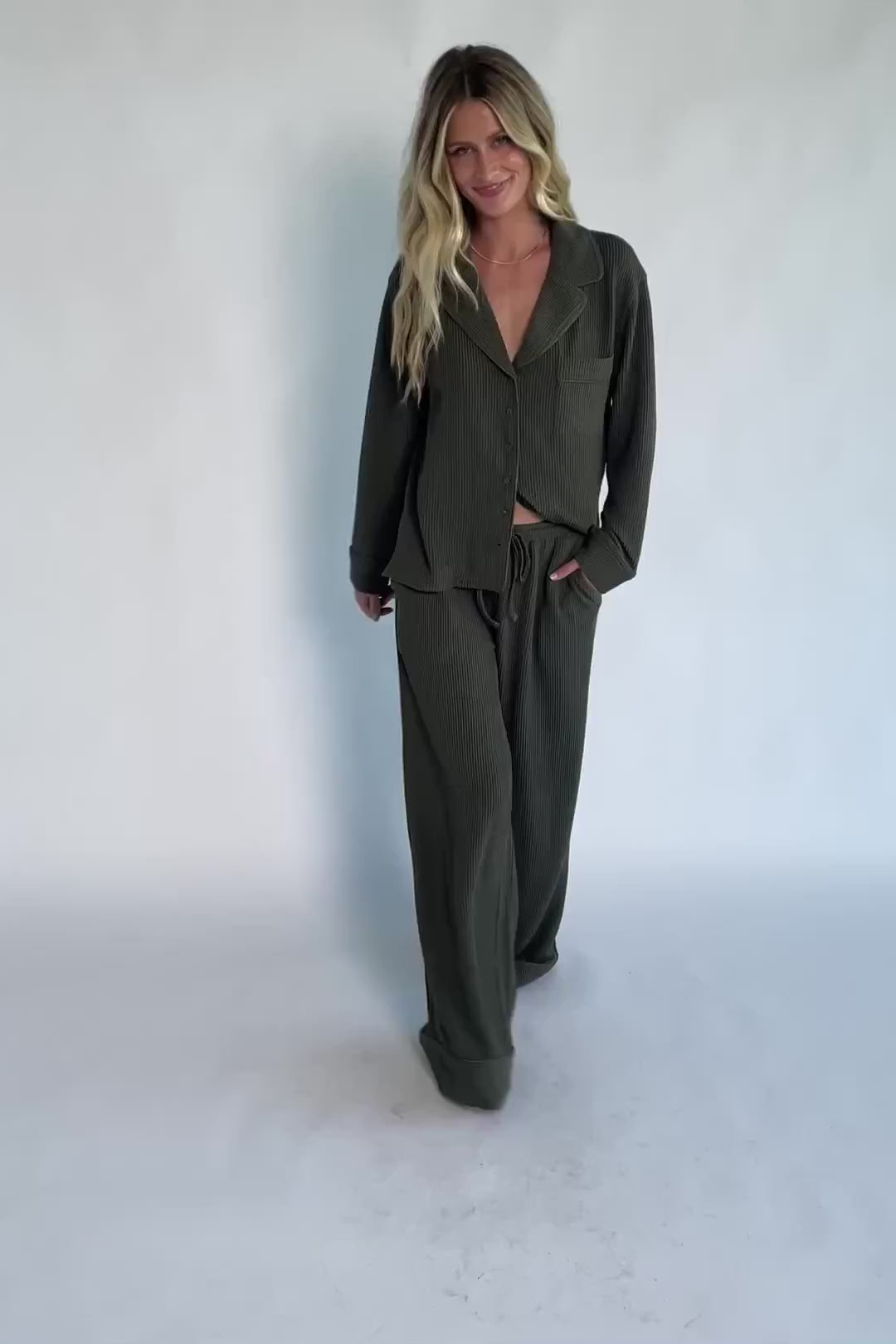 Model wearing a ribbed knit pajama set featuring a long-sleeve button-front V-neck top with a chest pocket and matching wide-leg pants with an elastic drawstring waist for a cozy, relaxed silhouette.