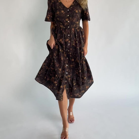 Clove floral midi dress with a V-neckline, functional button-front closure, puff sleeves, elastic back waist, side pockets, and a tiered skirt.