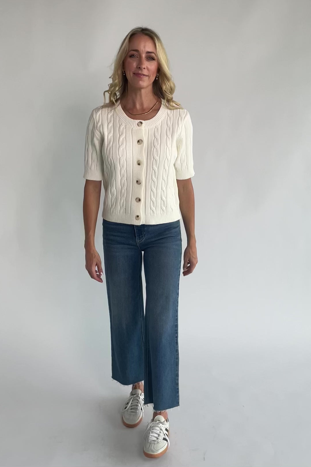 Cream cable knit cardigan with a round neckline, button-front closure, short sleeves, ribbed trim, and a fitted silhouette.