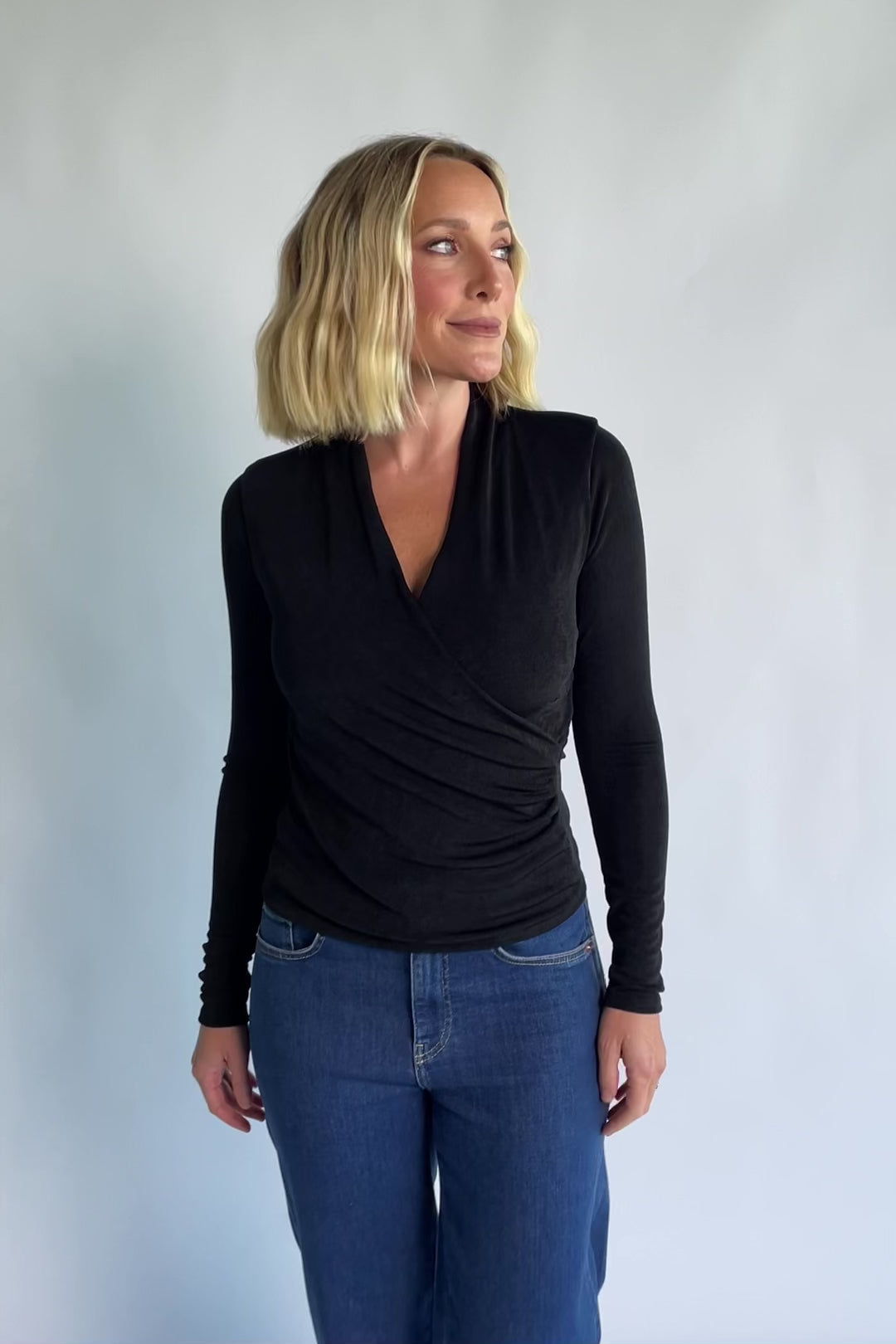 Aelia Top in Black with a plunging V-neckline, crossover front, and ruching along the side.
